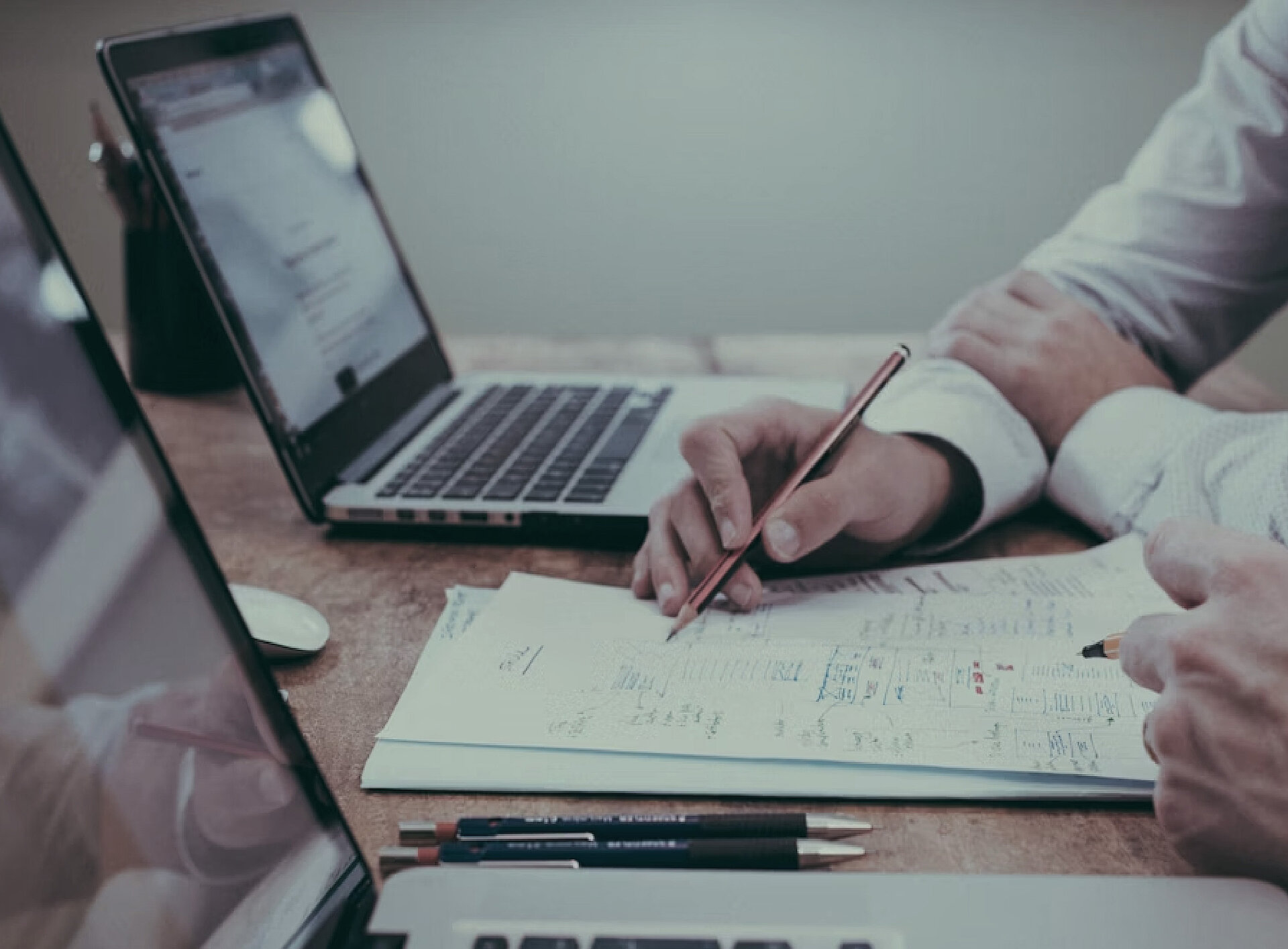 Eine Person notiert etwas auf einem Blatt Papier neben einem Laptop
